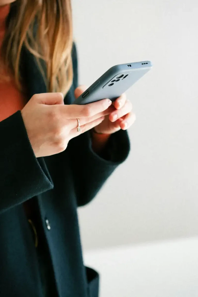 Žena v tmavém kabátu drží v rukou mobilní telefon